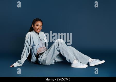 La jeune femme confiante brille dans sa tenue denim chic sur un fond solide. Banque D'Images