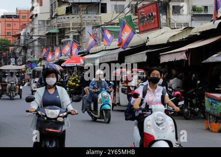 Phnom Penh, Cambodge - 25 juin 2022 : les motocyclistes, portant des masques faciaux en raison de la pollution de l'air et de la poussière, conduisent leurs scooters devant Toul Tom po Banque D'Images