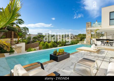 Superbe villa de golf de luxe, avec une élégante piscine à débordement, un mobilier de jardin moderne et un aménagement paysager vert sous un ciel bleu clair Banque D'Images