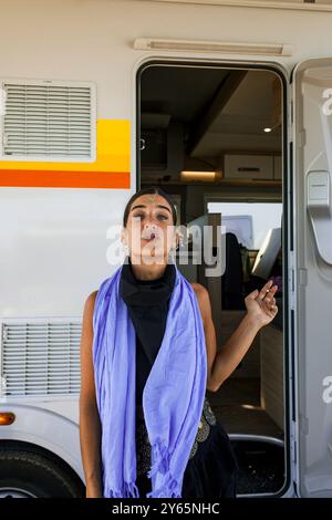 Une jeune femme se tient debout fumant à la porte d'un camping-car lors d'un festival de musique dans le désert de Monegros, regardant directement la caméra. Banque D'Images
