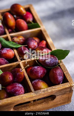 Gros plan de prunes mûres biologiques fraîches disposées dans une caisse en bois rustique, mettant en valeur les couleurs vives et la texture juteuse des fruits fraîchement récoltés Banque D'Images