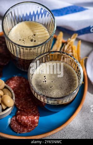 Boisson traditionnelle kvass dans des verres, accompagnée de poisson frit, de deux types de saucisses et de champignons fermentés présentés sur une plaque bleue vibrante avec un Banque D'Images