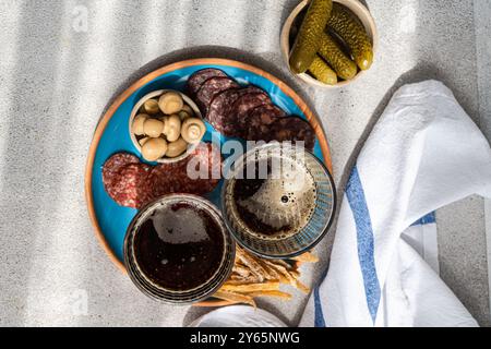 Boisson traditionnelle kvass servi dans des verres, accompagné de tranches de poisson frites, deux types de saucisses, champignons fermentés et concombres marinés sur un co Banque D'Images