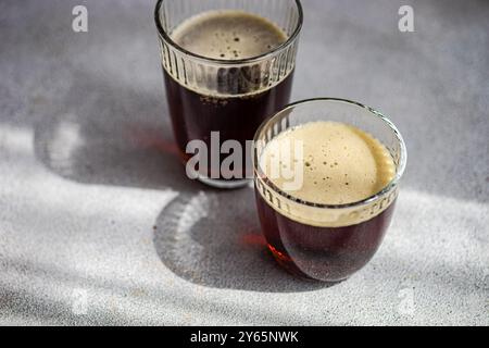 Deux verres remplis de kvass traditionnel, une boisson fermentée, reposent sur une surface claire, projetant de douces ombres contre le contraste de la boisson noire Banque D'Images