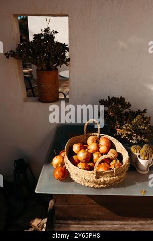 Une scène ensoleillée de grenades mûres dans un panier tissé positionné sur une table, encadrée par un cadre méditerranéen classique Banque D'Images