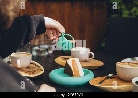 Personne coupée méconnaissable versant de la sauce caramel dans un cheesecake sur une assiette en céramique, capturée dans un café. Banque D'Images