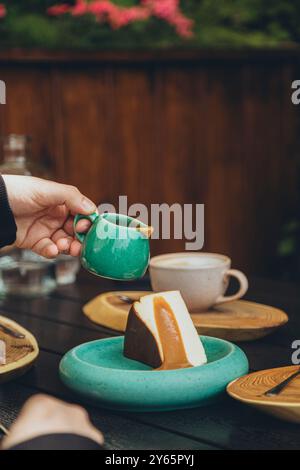 Personne coupée méconnaissable versant de la sauce caramel dans un cheesecake sur une assiette en céramique, capturée dans un café. Banque D'Images