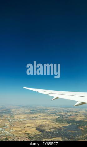 Une vue sereine du paysage ci-dessous vu d'en haut, avec un ciel dégagé et l'aile de l'avion en vue. Banque D'Images