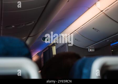 Un intérieur confortable de cabine d'avion avec compartiments supérieurs, éclairage doux et sièges passagers, capturant le confort des voyages aériens vu depuis le Banque D'Images