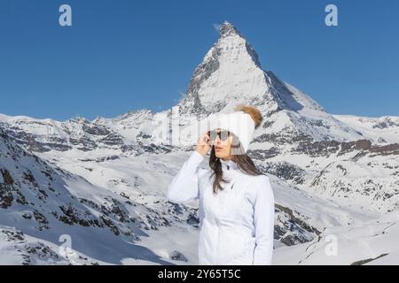 Une femme dans des vêtements d'hiver à la mode se tient devant la majestueuse montagne Matterhorn, mettant en valeur la mode hivernale moderne et chaude au milieu d'une vue à couper le souffle Banque D'Images