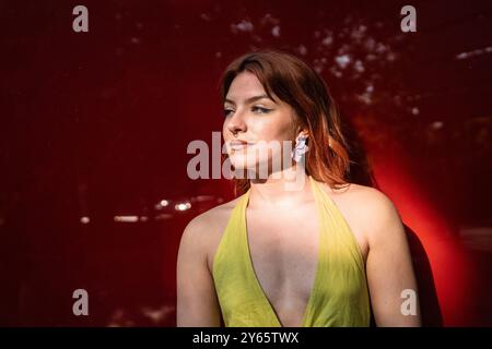 Portrait captivant d'une jeune femme aux cheveux roux et perçant le septum, vêtue d'une robe jaune éclatante à col ras du cou. Debout contre un u flou Banque D'Images