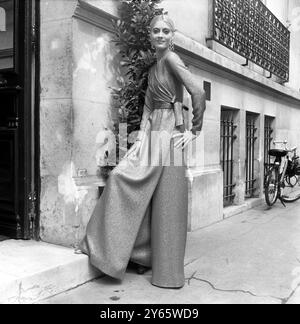 Dans sa collection muet , sobre pour l'hiver à venir Yves Saint Laurent a présenté des pantalons tout au long de ses mannequins de jour et de soirée . Cuivre lame mode cette robe de soirée avec de longues manches serrées, corsage enveloppant et jupe enveloppante portée avec un pantalon large du même tissu. D’énormes boucles d’oreilles en or compensent la sévérité de la coiffure avec son chignon pendant. 7 août 1968 Banque D'Images