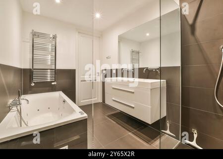 Cette image présente une salle de bains moderne spacieuse avec une baignoire jacuzzi, meuble-lavabo élégant, murs carrelés et luminaires élégants Banque D'Images