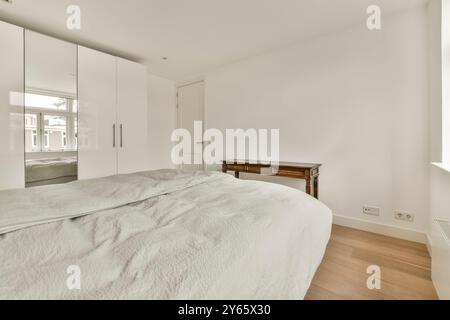 Cette chambre spacieuse et moderne dispose de draps blancs sur un grand lit, de parquet et d''un éclairage naturel lumineux Banque D'Images