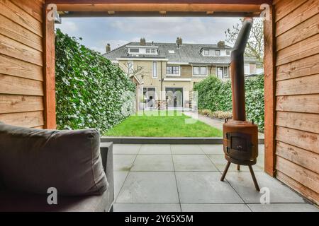 Une scène relaxante dans la cour comme vu d'un patio abrité, avec un poêle à feu moderne, pelouse verte, et maison en briques. Banque D'Images