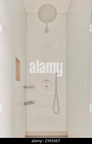 Une cabine de douche élégante et minimaliste avec une grande pomme de douche à effet pluie, une douche à main et des luminaires élégants sur un fond blanc propre. Banque D'Images