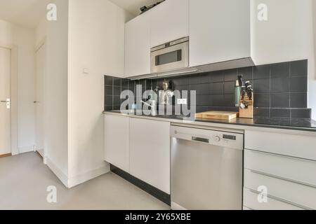 Un intérieur de cuisine élégant et moderne avec des armoires blanches, des carreaux noirs et des appareils en acier inoxydable. Banque D'Images