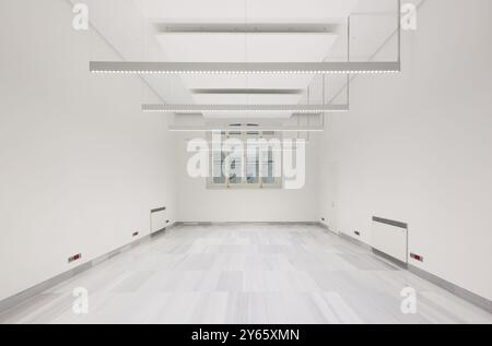 Un vaste espace de bureau minimaliste attend la personnalisation, avec un éclairage LED lumineux et un intérieur blanc immaculé. Banque D'Images
