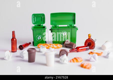 Deux poubelles vertes miniatures ouvertes et divers déchets jetés éparpillés autour, mettant en évidence la gestion et le recyclage des déchets. Banque D'Images