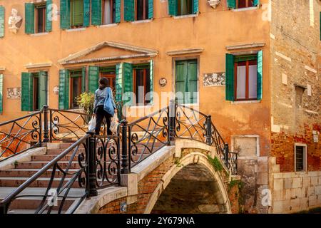 Une femme portant des sacs à provisions traverse Ponte Storto, un pont canal qui traverse le Rio Terà Sant' Aponal dans le sestieri San Polo de Venise, en Italie Banque D'Images