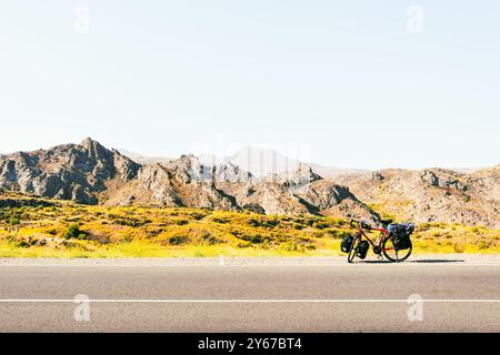 Chargé de sacs, des stands de vélo rouges sur le côté de la route entourée de vaches dans une campagne du parc national de Kazbegi. Vacances à vélo. Banque D'Images