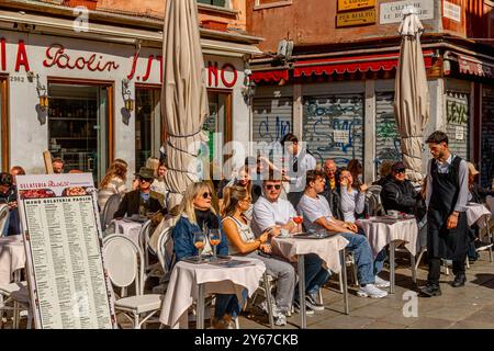 Les personnes assises dehors appréciant des boissons dans le soleil de printemps à Gelateria Paolin à Campo Santo Stefano dans le sestiere San Marco de Venise, Italie Banque D'Images