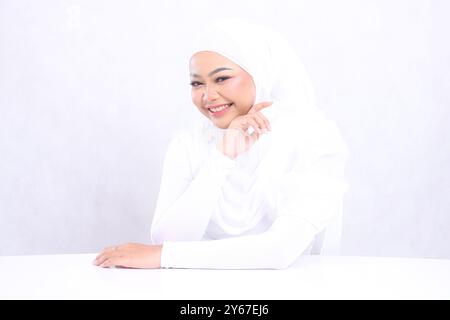 foulard de femme de beauté riant à la caméra avec une peau blanche parfaite et saine, les mains sur la table et les joues touchant le fond blanc isolé. visage de fille Banque D'Images