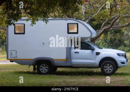 Camping-car blanc, camping-car, camping-car, garé dans un camping boisé sous un arbre de corail à la lumière du soir Banque D'Images