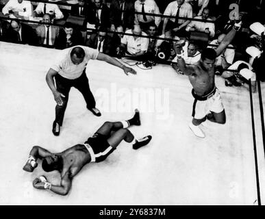 Le champion du monde des poids lourds, Muhammad Ali fait la tour d'un Sonny Liston déchu, au premier tour de leur combat pour le titre à Lewiston, dans le Maine. Clay a assommé Liston au premier tour pour garder sa couronne. L'arbitre Joe Walcott regarde. Clay a été déclaré vainqueur après une apparente confusion entre l'arbitre Walcott et un officiel du ring chargé de compter pour les knock-down. 25 mai 1965. Banque D'Images