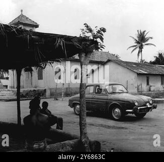 Route de rallye à travers les villages indigènes. Côte d'Ivoire, Afrique de l'Ouest. Comme les autochtones le regardent, une Renault Dauphine passe par le village de Banco, près d’Abidjan, lors des entraînements du 5ème Rallye de Côte d’Ivoire, organisé par l’automobile Club de Côte d’Ivoire. Le rallye a débuté hier à Abidjan, et après avoir parcouru une distance de quelque 1 488 km, les concurrents arriveront aujourd’hui à Abidjan pour l’arrivée. 22 février 1959. Banque D'Images
