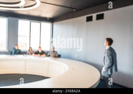 Vue floue sur une salle d’affaires avec une grande table ronde, l’orateur se tient devant le public. Formation commerciale ou conférence à l'université. Banque D'Images