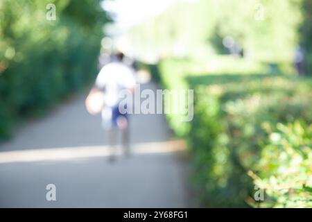 Arrière-plan flou, homme anonyme marchant le long de la route dans le parc. Journée ensoleillée d'été, Banque D'Images