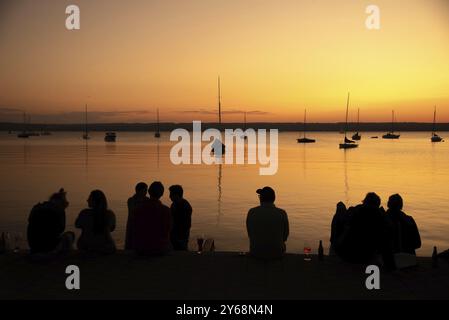 Les gens assis sur la rive du lac Ammer près de Herrsching, Bavière, Allemagne au coucher du soleil avec la lueur du coucher du soleil Banque D'Images