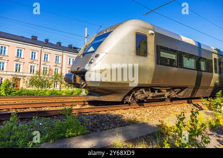 Train moderne à grande vitesse passant par une zone résidentielle en plein soleil. Suède. Banque D'Images