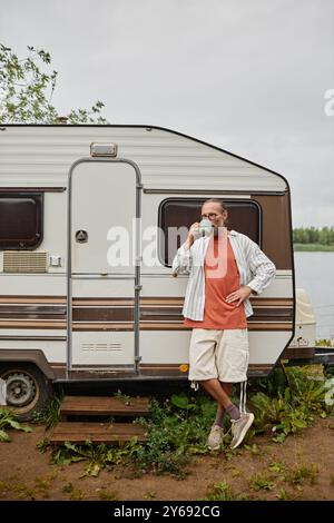 Portrait vertical pleine longueur de l'homme senior moderne profitant d'une tasse de café debout par van à l'extérieur dans la nature Banque D'Images