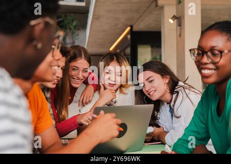 Groupe diversifié d'étudiants adolescents étudiant ensemble dans une bibliothèque, collaborant à un projet à l'aide d'un ordinateur portable, favorisant le travail d'équipe et la communication. Camarades de classe faisant une recherche avec un ordinateur. Photo de haute qualité Banque D'Images