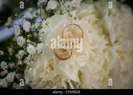 Élégantes bagues de mariage reposant sur un arrangement floral crémeux avec des accents blancs délicats. Banque D'Images