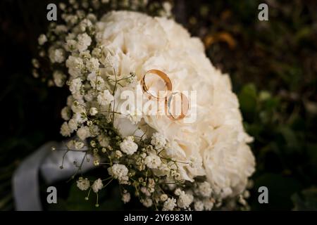 Élégantes bagues de mariage reposant sur un bouquet luxuriant de fleurs blanches. Banque D'Images