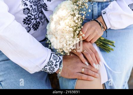 Gros plan romantique des mains du couple entrelacées avec un beau bouquet de mariage dans un cadre naturel. Banque D'Images