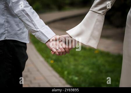 Gros plan romantique des mains entrelacées de mariée et mariée sur un chemin serein. Banque D'Images