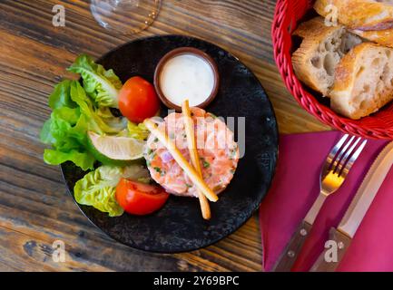 Tartare de saumon avec sauce à la ciboulette, tomates, laitue, citron vert et bâtonnets de pain Banque D'Images