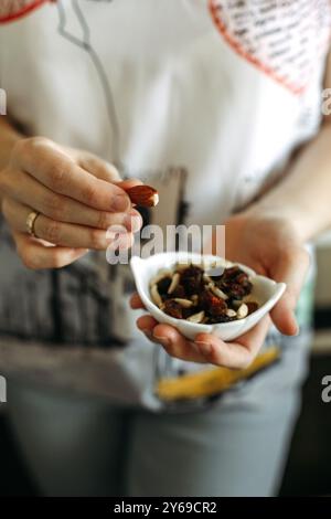 Tenant doucement une noix, une personne prend un moment pour profiter d'une collation saine à partir d'un petit plat, entouré d'une ambiance de cuisine chaleureuse et de lumière douce du soleil. Banque D'Images