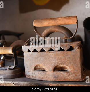 Antique, fer plat en acier, également appelé fers triste, se trouve sur une étagère en bois. Il a un dessus articulé pour mettre les charbons dedans pour le repassage. La poignée est en bois. Banque D'Images