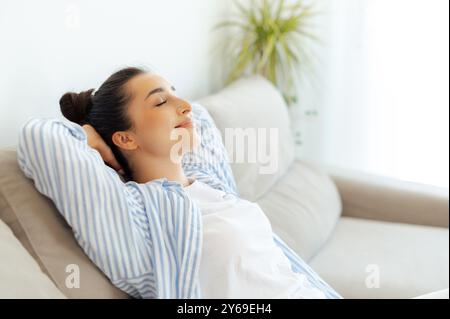 Pas de stress, détendez-vous. Heureuse femme indienne ou arabe calme se reposant sur un canapé confortable à la maison seule dans le salon, fermé ses yeux rêvant ou prenant la sieste de jour, profitant du temps libre le week-end, souriant Banque D'Images