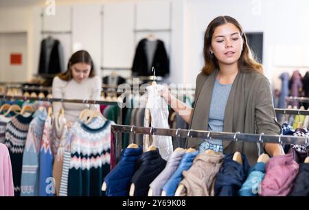 Jeune consommateur féminin choisissant des vestes coupe-vent dans le centre commercial Banque D'Images