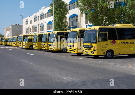 Plusieurs autobus scolaires jaunes sont alignés devant l’école, prêts à venir chercher des élèves à abu dhabi Banque D'Images