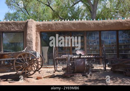 Wagon et charrue sont assis à l'extérieur du Casa Grade Trading Post à Cerrillos, Nouveau-Mexique. La fenêtre affiche un ensemble de bouteilles. Banque D'Images