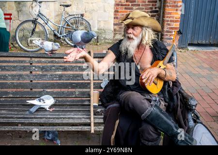 Un artiste de rue en costume de pirate est assis sur Un banc public nourrissant des pigeons, High Street, Lewes, Sussex, Royaume-Uni. Banque D'Images