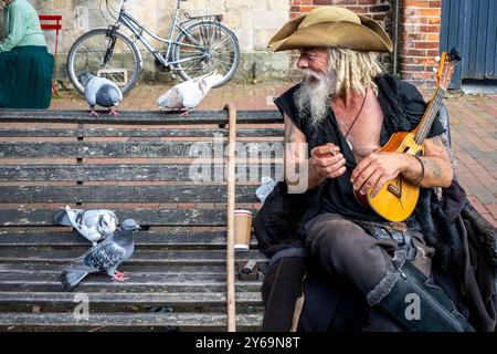 Un artiste de rue en costume de pirate est assis sur Un banc public nourrissant des pigeons, High Street, Lewes, Sussex, Royaume-Uni. Banque D'Images