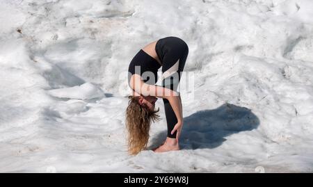 Personne féminine pratiquant le yoga en plein air dans la neige, exécutant la posture Standing Forward Bend Uttanasana, avec la tête abaissée vers les jambes et h. Banque D'Images